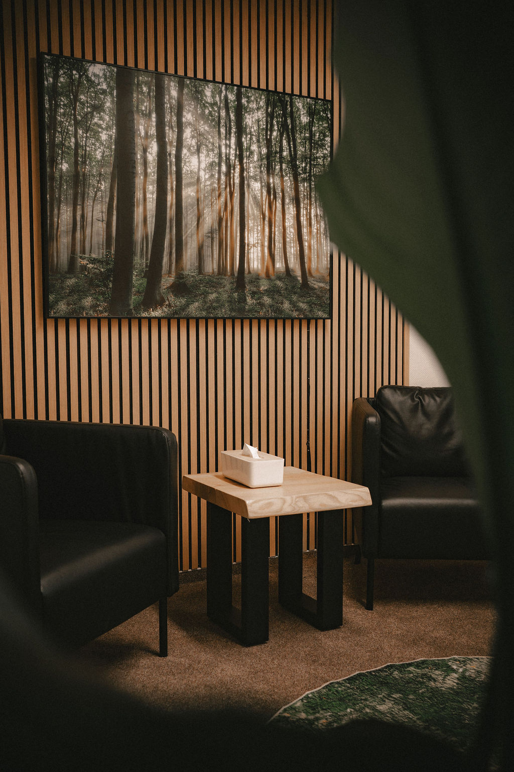 Zwei schwarze Sessel stehen neben einem Tisch mit einer holzähnlichen Oberfläche und Kunstwerk im Hintergrund.